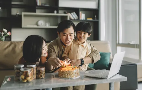 parents with a child celebrating a birthday with a small cake in their living room