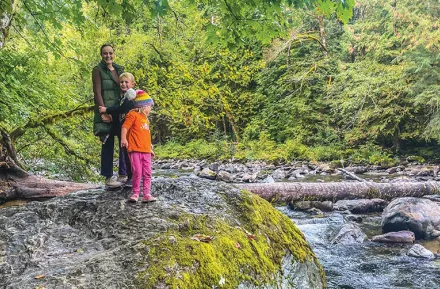 Mom and two children standing on a large rock next to a river at Twin Falls is a good winter hike near Seattle