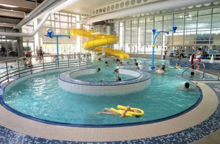View of people swimming in Rainier Beach indoor Pool in Seattle. Yellow twister slide is in the background and the lazy river feature is in the foreground