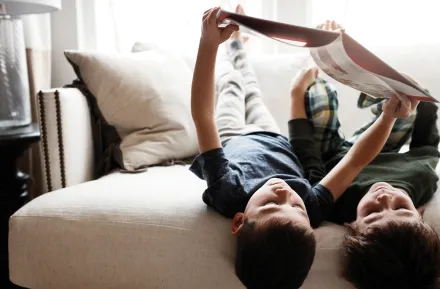 Brothers reading a book together on a couch upside-down 