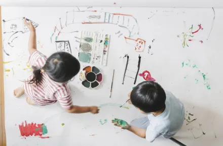 Two siblings painting on butcher paper together