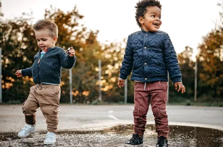 Two little kids playing in a puddle at a park on a rainy day