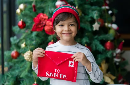 child under a Christmas tree holding a letter for Santa