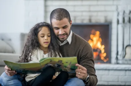 Dad and daughter reading in front of fireplace