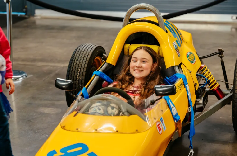 Girl sitting in a yellow race car at America’s Car Museum