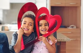 Two kids with paper hearts by their faces and useful Valentine's Day favors