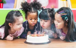 Little girls around a birthday cake blowing out the candles 