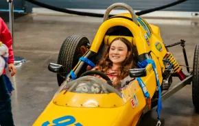 Girl sitting in a yellow race car at America’s Car Museum