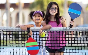 Two girls smiling on a summer day on a pickleball court near Seattle, one of many sports activities to try