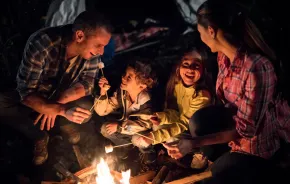 Families around a campfire roasting marshmallows and playing a campfire game