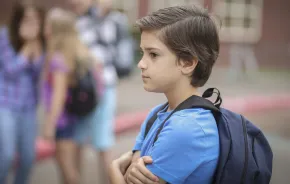 Boy standing alone next to a group of kids, ADHD and lacking social capital. 