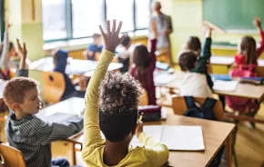 Classroom at school full of students, several raising their hands to answer a question