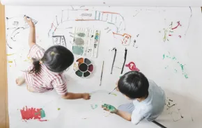 Two siblings painting on butcher paper together