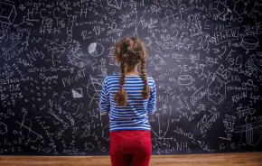 child standing looking at a blackboard covered with math