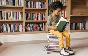 child sitting on a stack of books reading