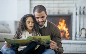 Dad and daughter reading in front of fireplace