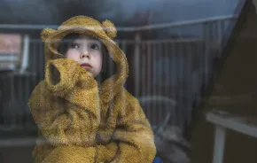 child in a bear hoodie looking out a window experiencing winter burnout