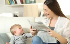 mom and baby sitting on the couch mom reading the newspaper